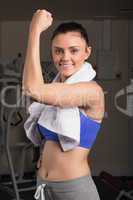 Young woman with towel flexing muscles in gym