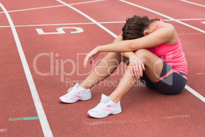 Tensed sporty woman sitting on the running track