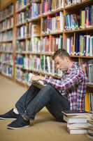 Serious student sitting on library floor reading