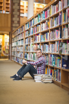 Cheerful student sitting on library floor reading