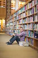 Cheerful student sitting on library floor reading