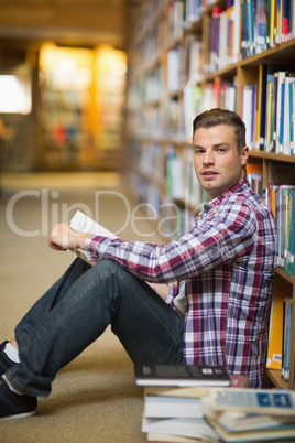 Handsome student sitting on library floor reading
