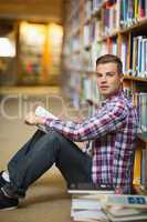 Handsome student sitting on library floor reading