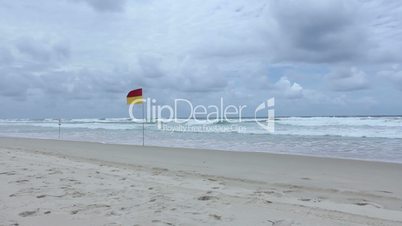 Lifeguard flag on sunny Gold Coast beach with Surfers Paradise in the background, Australia.