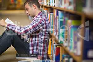 Focused young student sitting on library floor reading