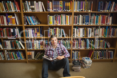 Smiling young student sitting on library floor reading