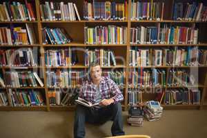 Smiling young student sitting on library floor reading