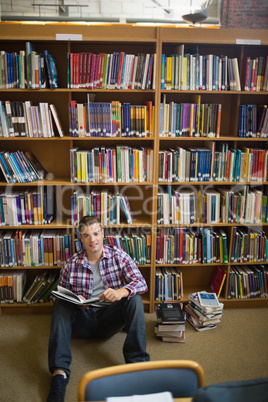 Happy young student sitting on library floor reading