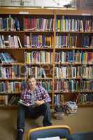 Happy young student sitting on library floor reading