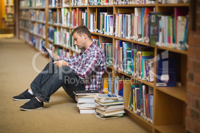 Focused young student sitting on library floor using tablet