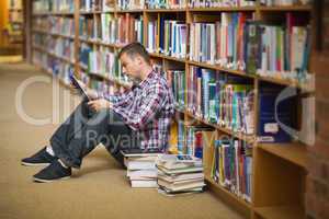 Focused young student sitting on library floor using tablet