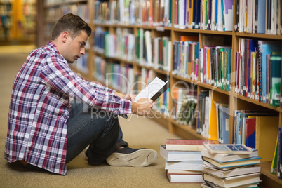 Handsome young student sitting on library floor reading book