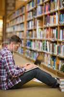 Handsome young student sitting on library floor using laptop