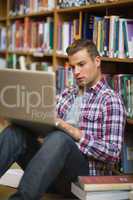 Focused young student sitting on library floor using laptop