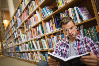 Focused young student sitting on library floor reading book