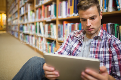 Serious young student sitting on library floor using tablet