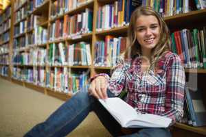 Happy pretty student sitting on library floor reading book