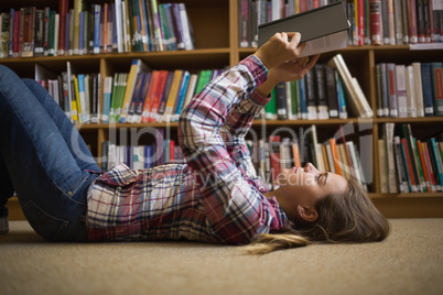 Pretty student lying on library floor reading book