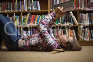 Pretty student lying on library floor reading book