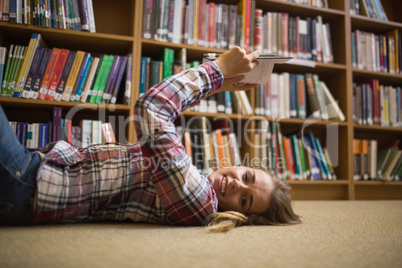 Pretty happy student lying on library floor reading book