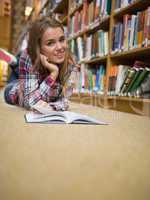 Young cheerful student lying on library floor reading book