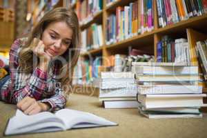Young happy student lying on library floor reading book