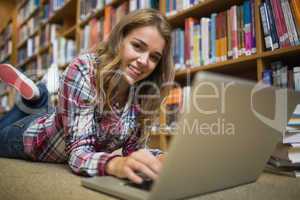 Young smiling student lying on library floor using laptop