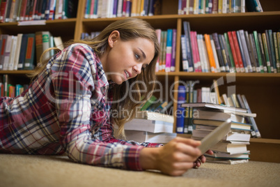 Young student lying on library floor using tablet pc