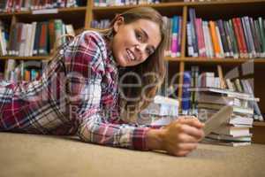 Smiling student lying on library floor using tablet pc