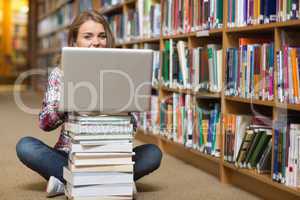 Happy student sitting on library floor using laptop on pile of b