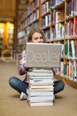 Smiling student sitting on library floor using laptop on pile of