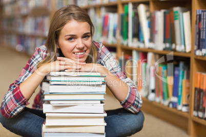 Smiling student sitting on library floor leaning on pile of book