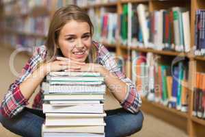 Smiling student sitting on library floor leaning on pile of book