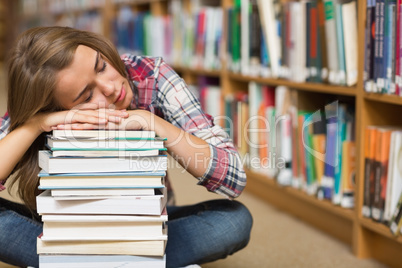 Sleeping student sitting on library floor leaning on pile of boo