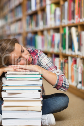 Napping student sitting on library floor leaning on pile of book