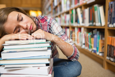 Dozing student sitting on library floor leaning on pile of books