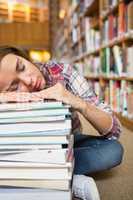 Dozing young student sitting on library floor leaning on pile of