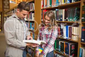 Happy classmates standing in library talking about a book