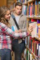 Pretty student taking book from shelf in library