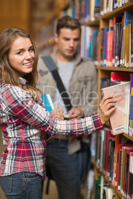 Smiling student taking book from shelf in library