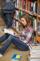 Focused student reading book on library floor