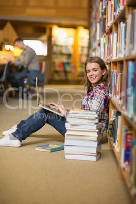 Happy student using laptop on library floor looking at laptop