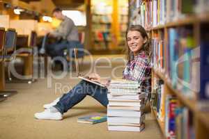 Smiling student using laptop on library floor looking at laptop