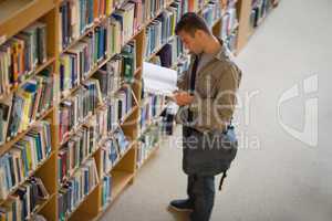 Student reading a book from shelf in library