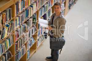 Student holding a book from shelf in library smiling at camera