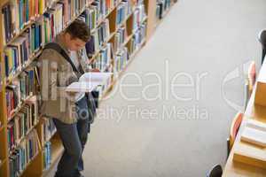 Student reading a book from shelf standing in library