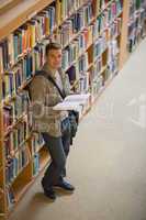 Student reading a book standing in library smiling at camera