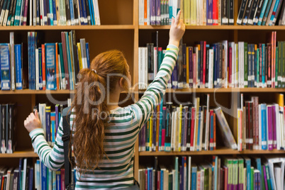 Redhead student taking book from top shelf in library