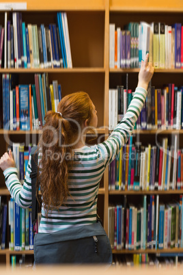 Redhead student taking book from shelf in library