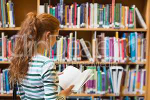 Redhead student reading book from shelf in library